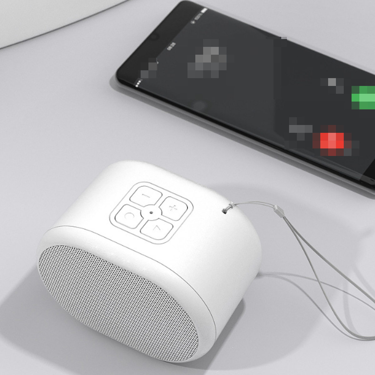 Weißer Lautsprecher mit Knöpfen neben einem schwarzen Smartphone auf grauer Oberfläche.