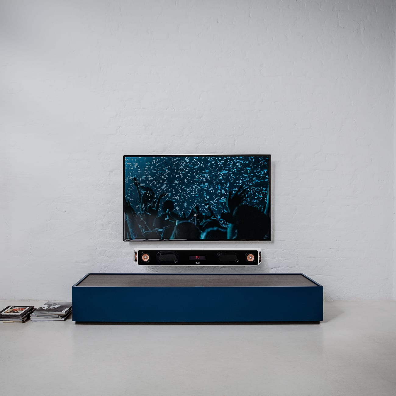 Fernseher an einer weißen Backsteinmauer mit Soundbar darunter. Ein blauer Schrank ist darunter.