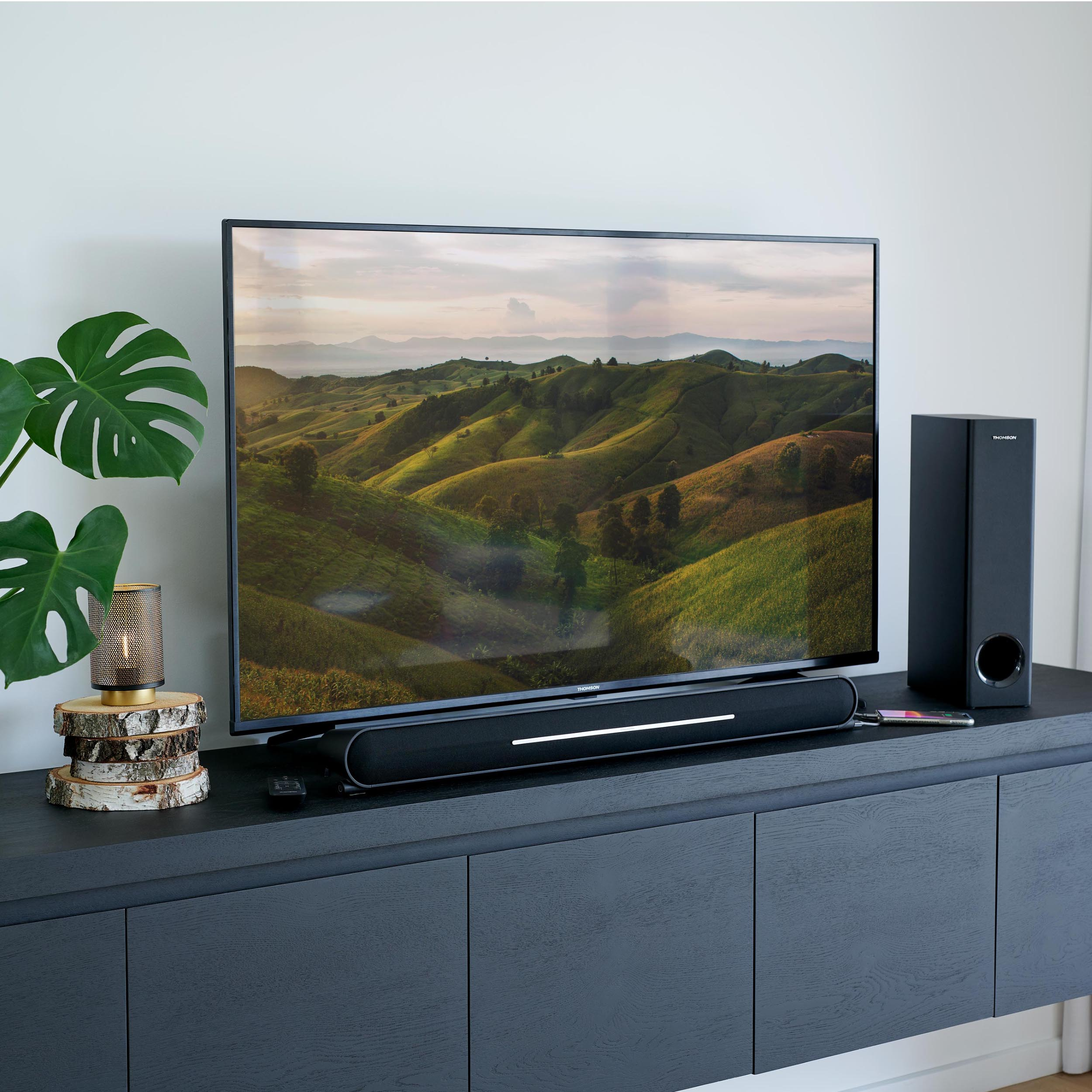 Telewizor ze sceną krajobrazową na ekranie, soundbarem i głośnikiem.