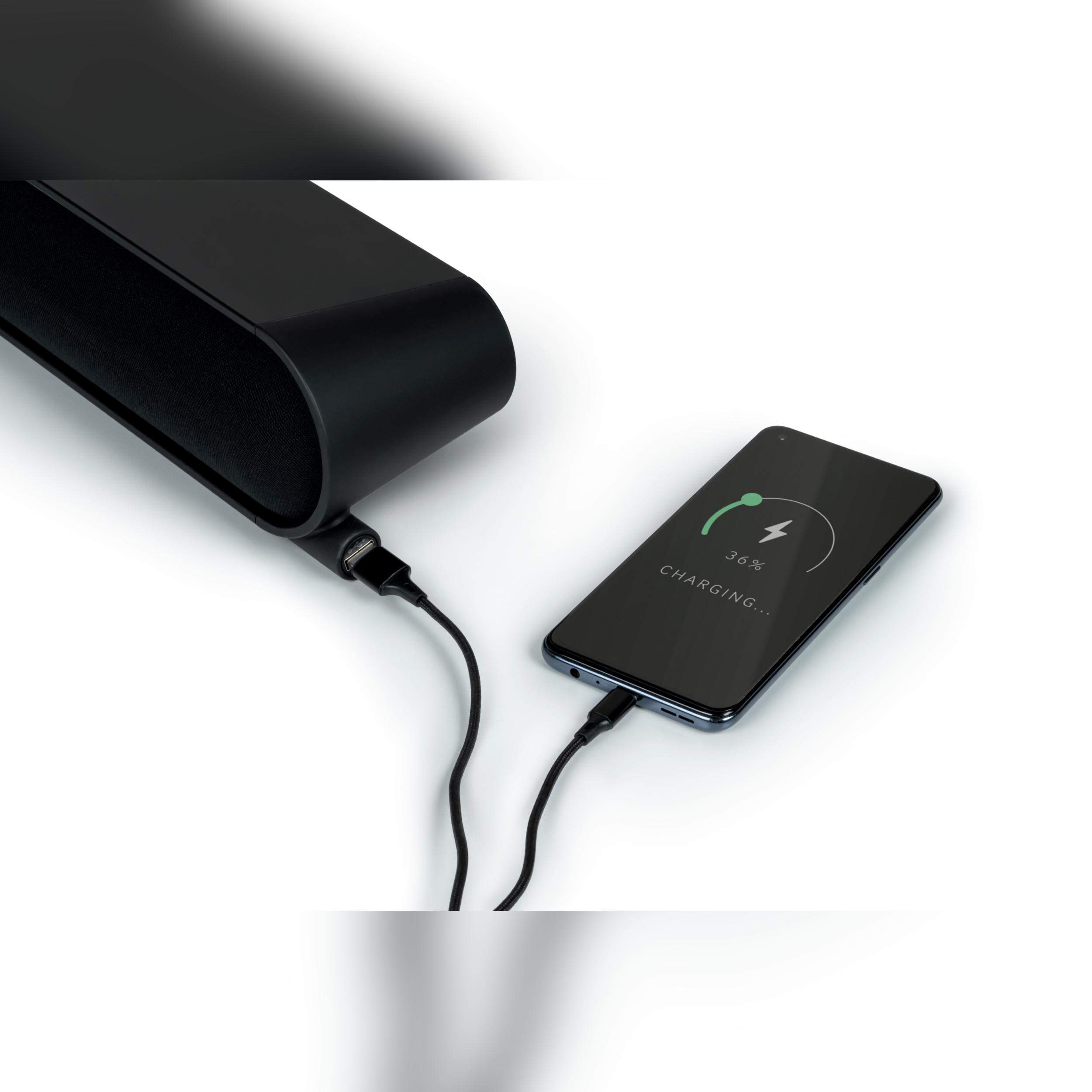 Czarny głośnik i ładowanie telefonu. Telefon naładowany w 36%. Białe tło.