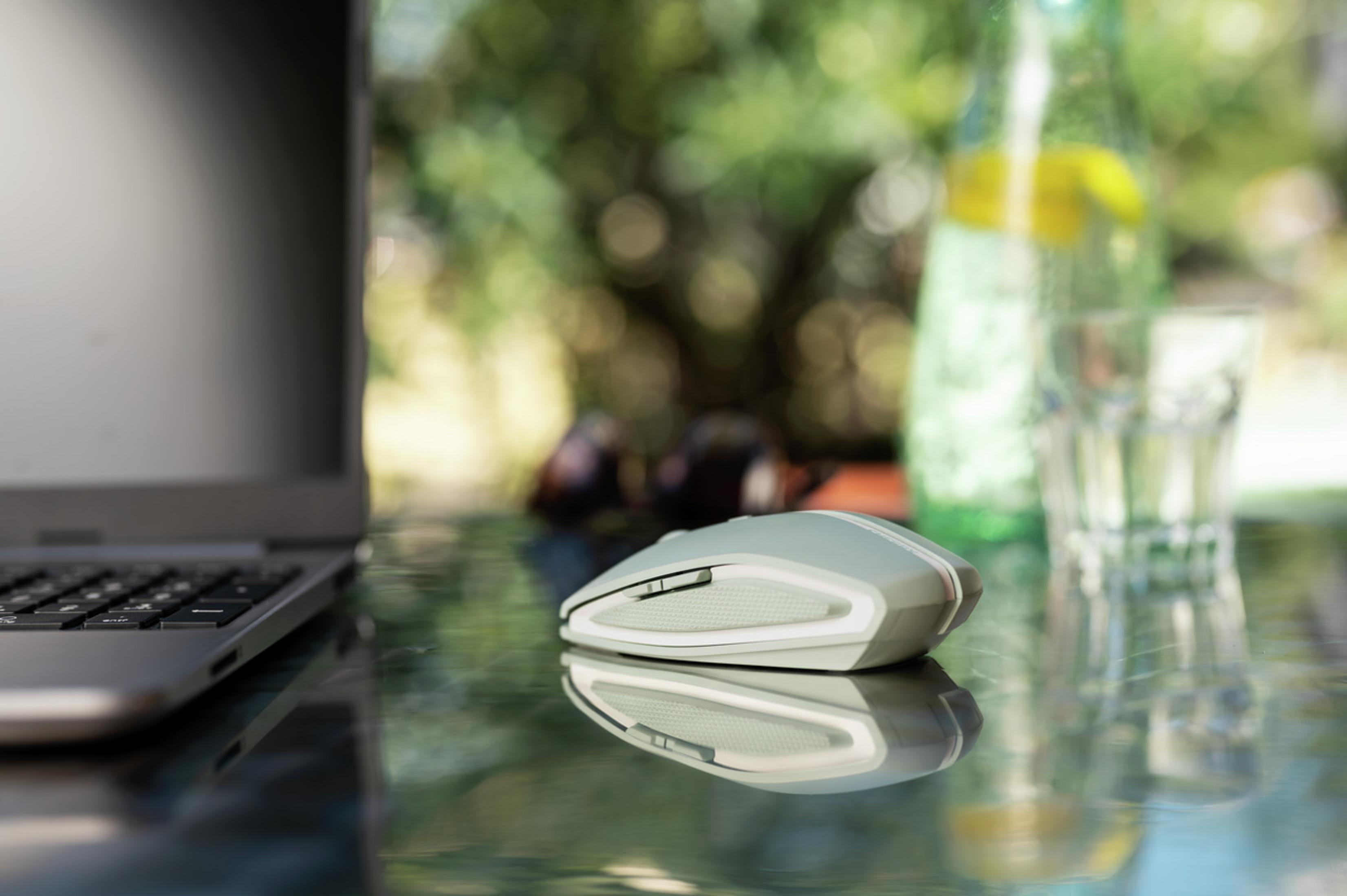 Eine Computermaus, ein Laptop, eine Wasserflasche und ein Glas auf einer reflektierenden Oberfläche.