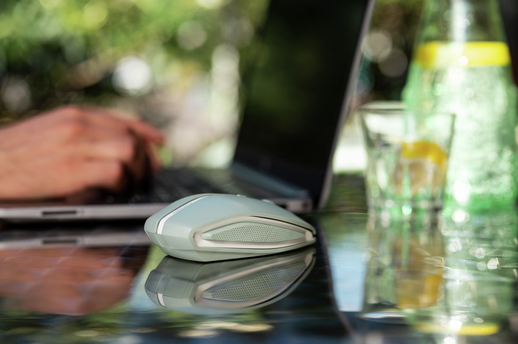 Laptop auf einem Glastisch mit Maus. Glas Wasser und Flasche im Hintergrund.