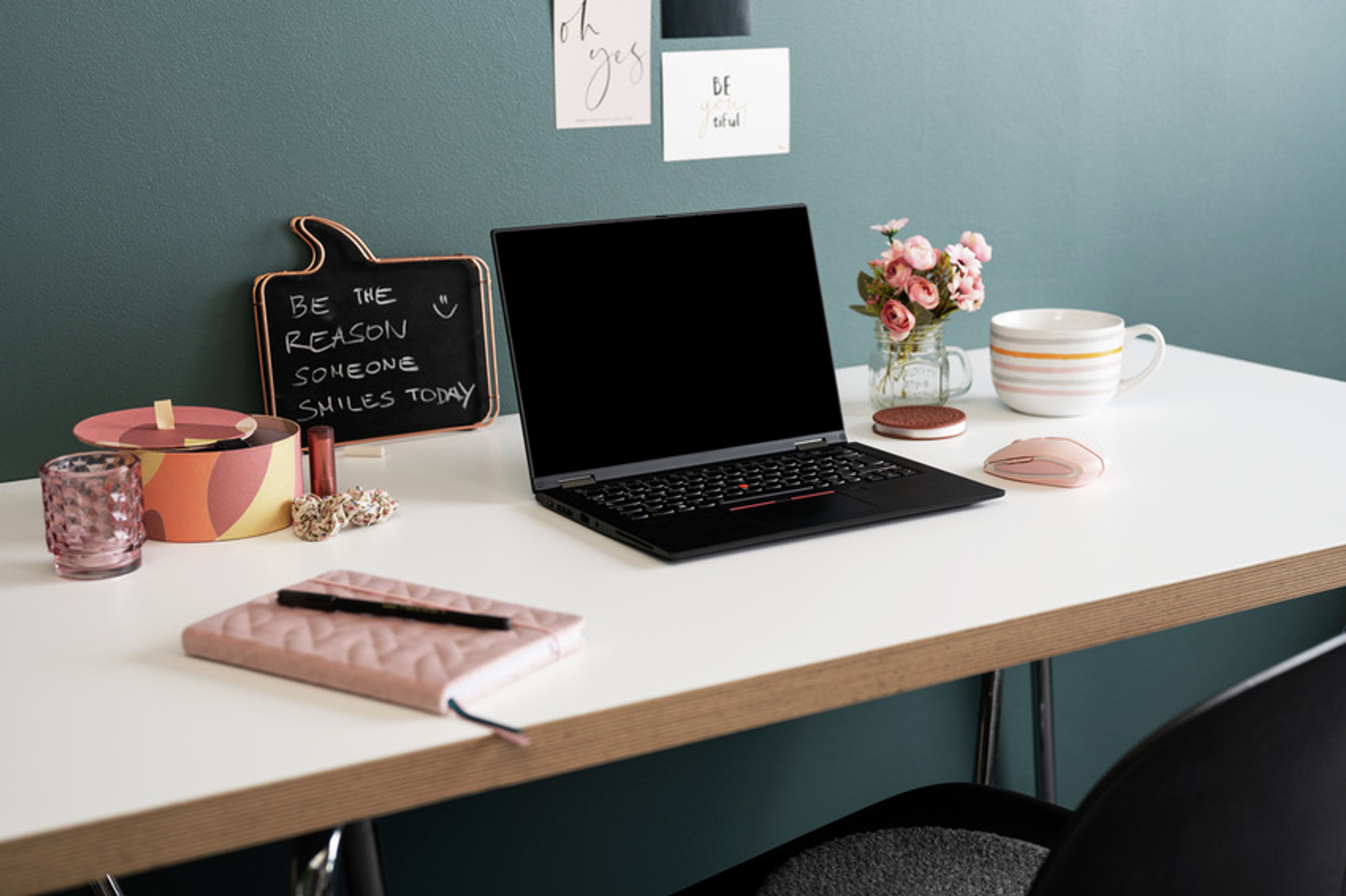 A desk with a laptop, flowers, a mug, a mouse, and stationery.