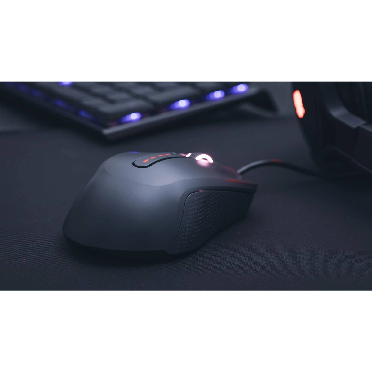 Mouse da gaming nero su un tappetino nero, mostra luce rossa e una tastiera sullo sfondo.