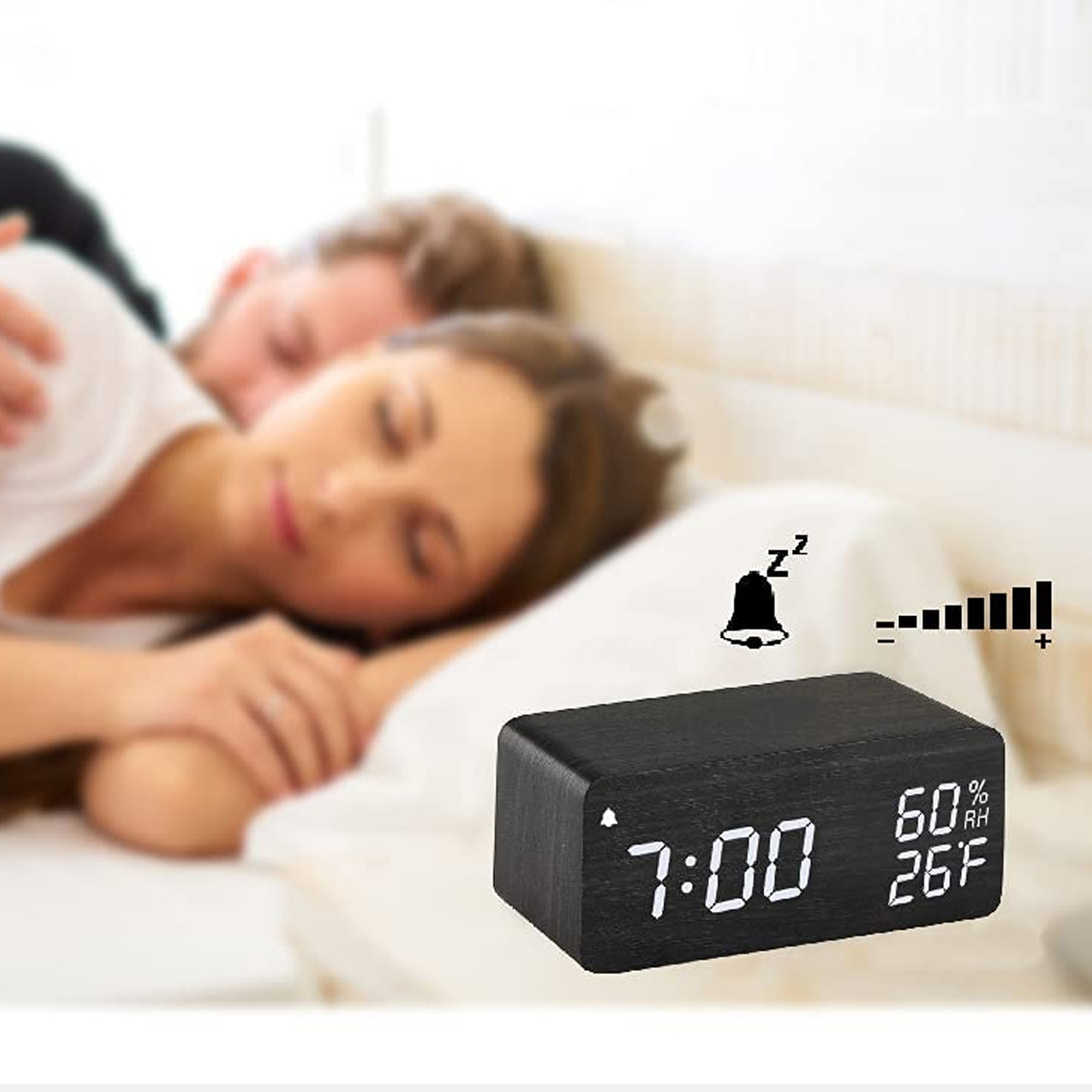 Ein schwarzer Wecker zeigt 7:00, 60 % RH, 26F. Ein Paar schläft in einem Bett.
