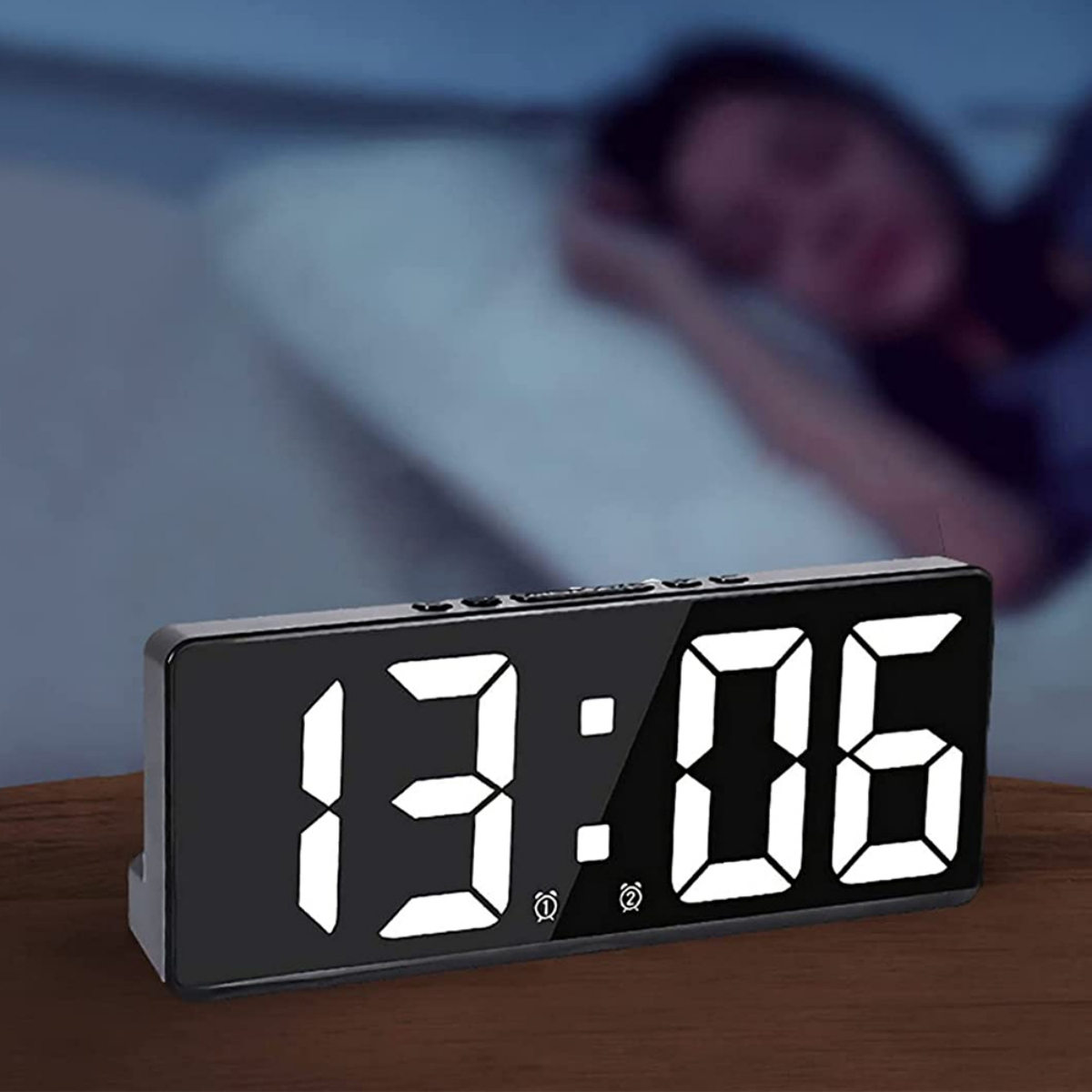 Schwarzer digitaler Wecker mit der Anzeige 13:06. Person schläft im unscharfen Hintergrund.