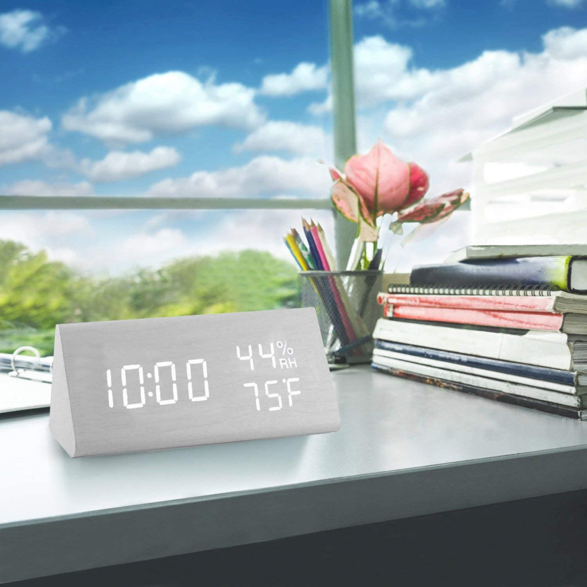 Digitaluhr auf einem Schreibtisch. Zeigt Zeit, Luftfeuchtigkeit und Temperatur. Fenster im Hintergrund.