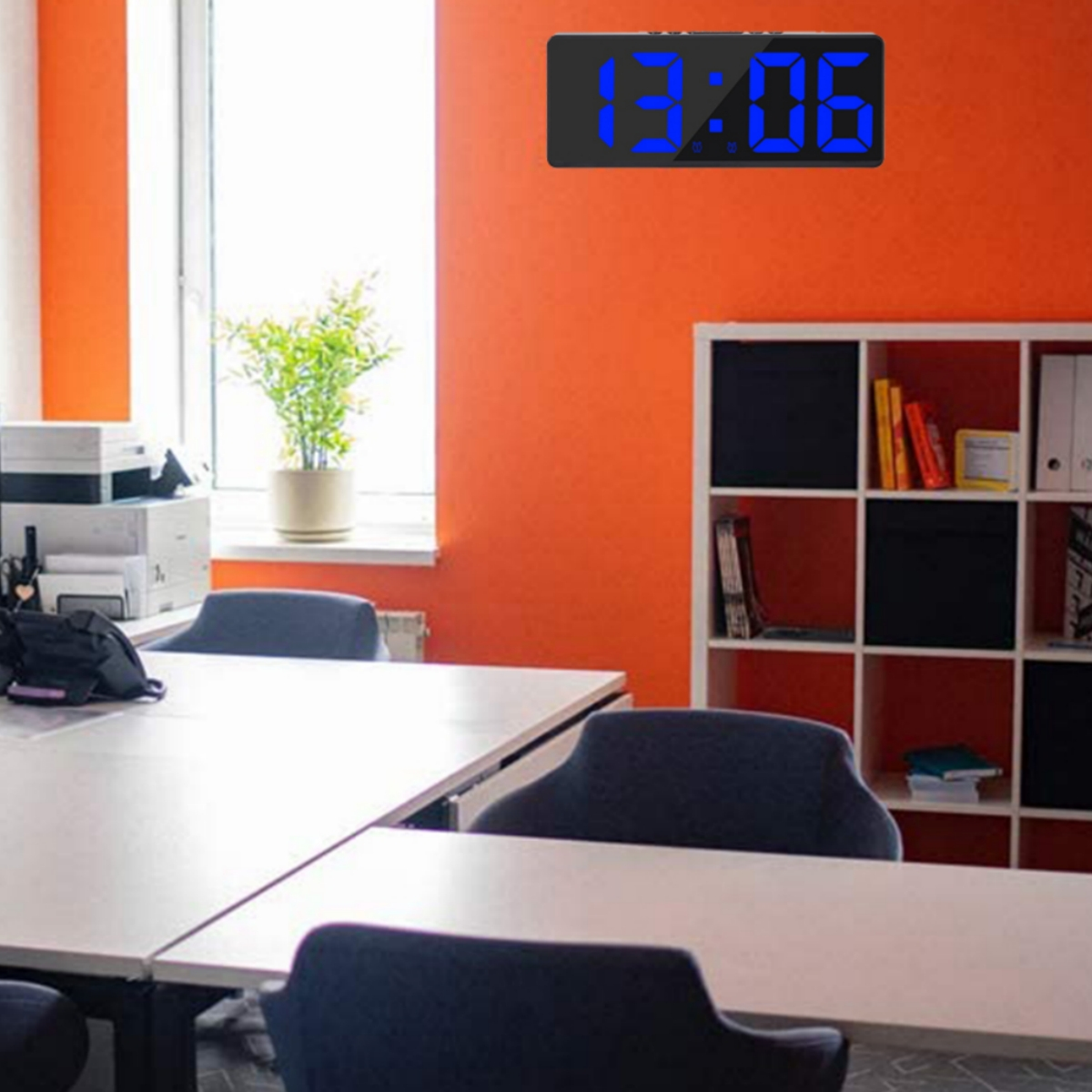 Büroraum mit digitaler Uhr an der orangefarbenen Wand, Tisch und Stühlen.