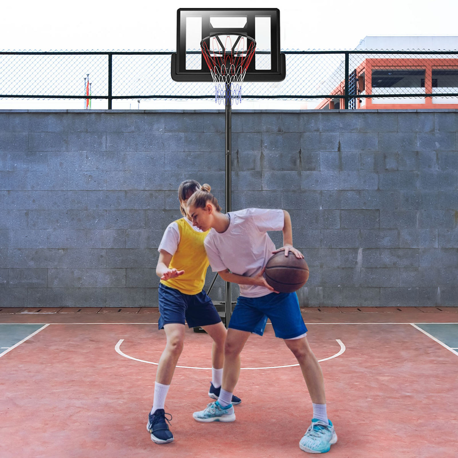 Zwei junge Männer spielen Basketball auf einem roten Platz. Einer hält den Ball, der andere verteidigt.