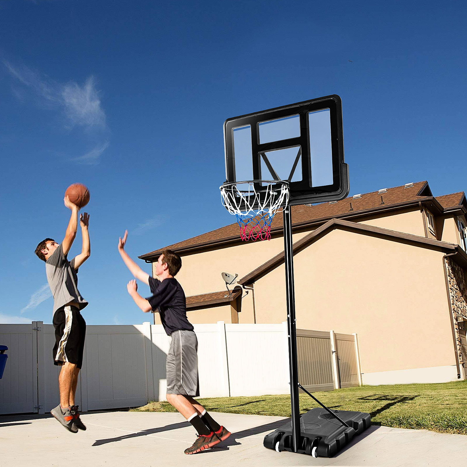 Zwei Jungen spielen Basketball auf einem Platz mit Korb. Blauer Himmel im Hintergrund.