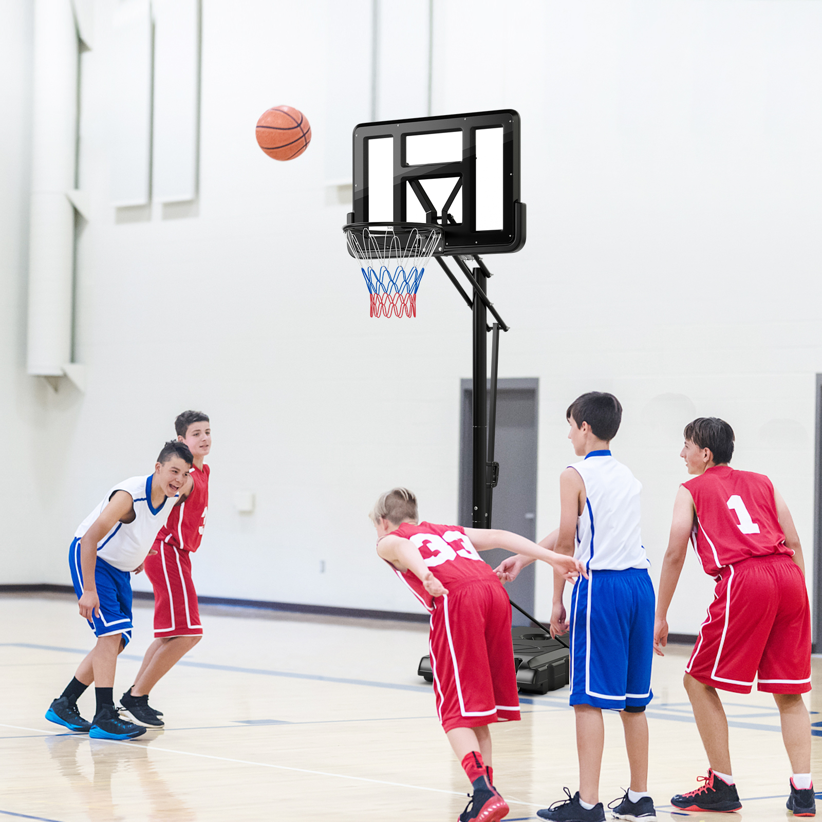 Basketballspiel im Gange. Spieler in roten und blauen Uniformen, Ball in der Luft, Korb im Hintergrund.