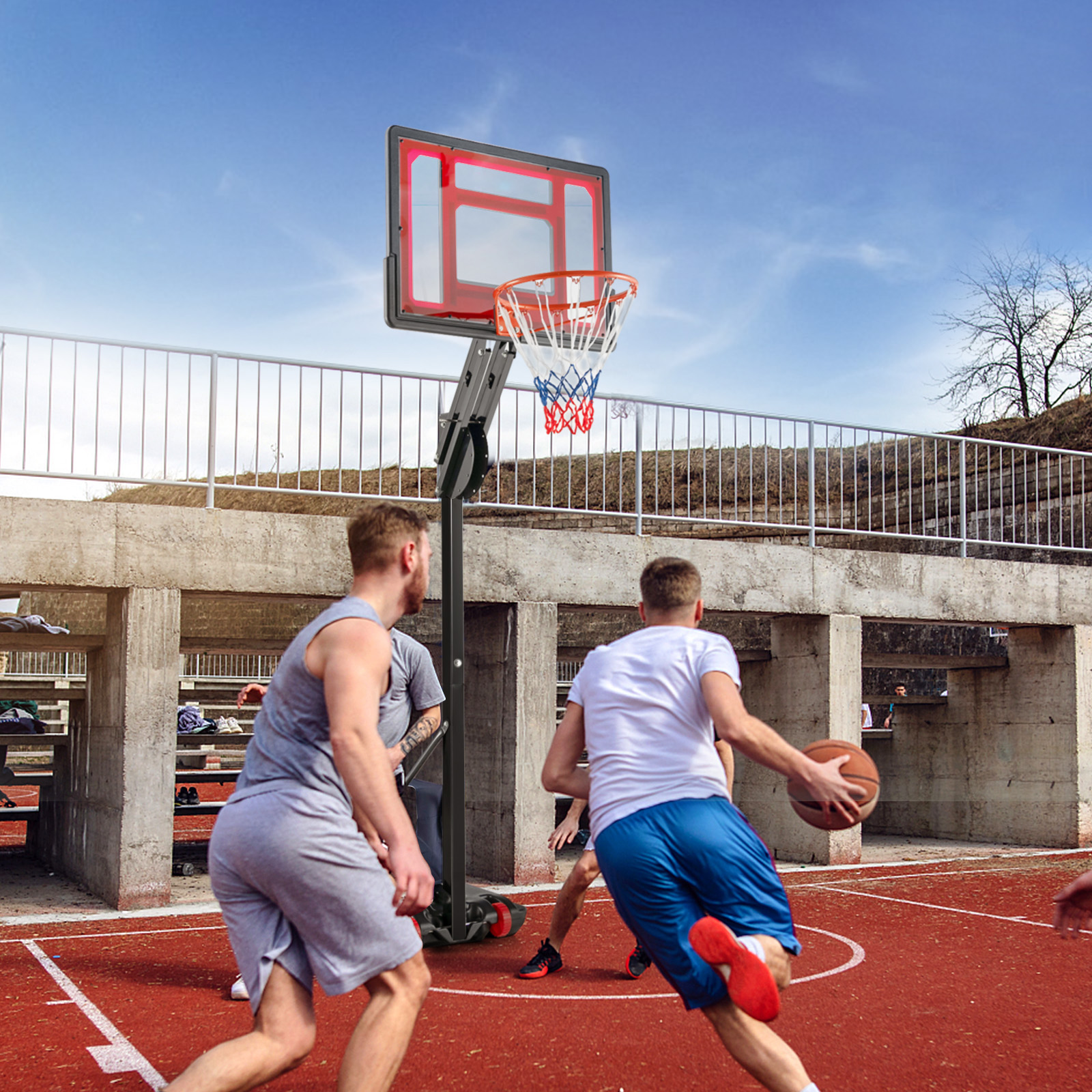 Leute spielen Basketball auf einem roten Platz mit einem Basketballkorb unter blauem Himmel.