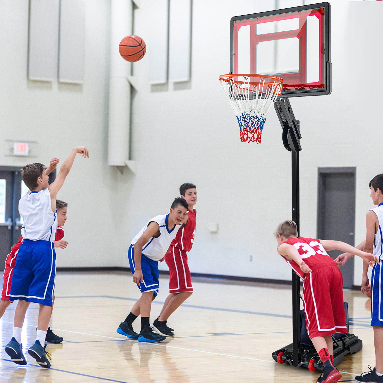 Kinder spielen Basketball, einer wirft, andere schauen zu, mit einem Basketballkorb in einer Turnhalle.