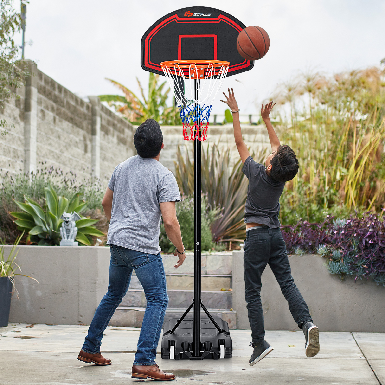 Ein Vater und ein Sohn spielen Basketball. Der Junge wirft, der Vater schaut zu. Basketballkorb im Hintergrund.
