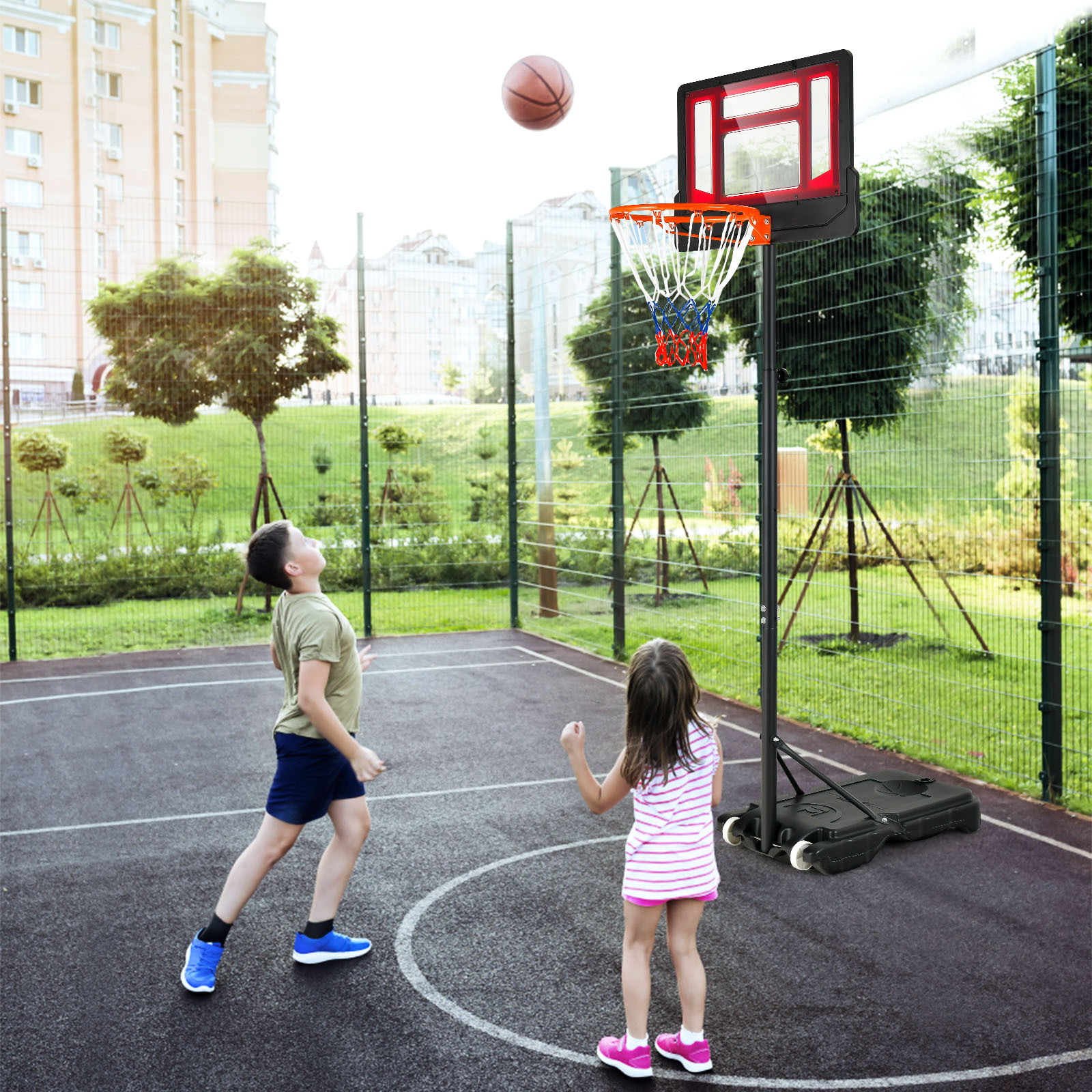 Zwei Kinder spielen Basketball. Ein Junge wirft, ein Mädchen schaut zu. Ein Basketballkorb steht im Hintergrund.