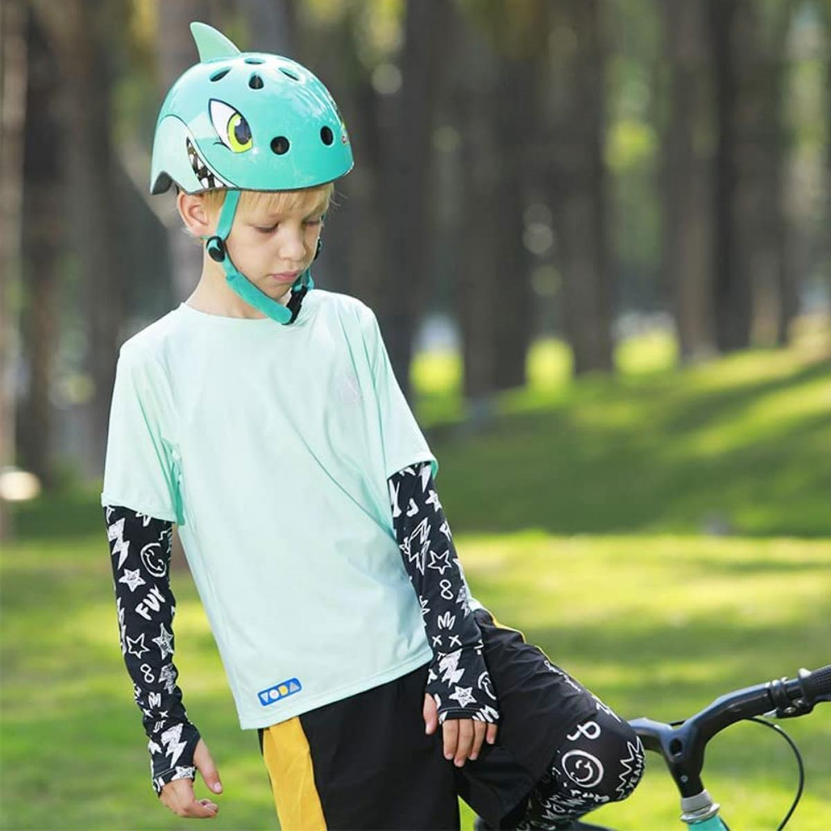 Junge mit Haihelm, blauem Shirt und Armschützern, fährt Fahrrad.