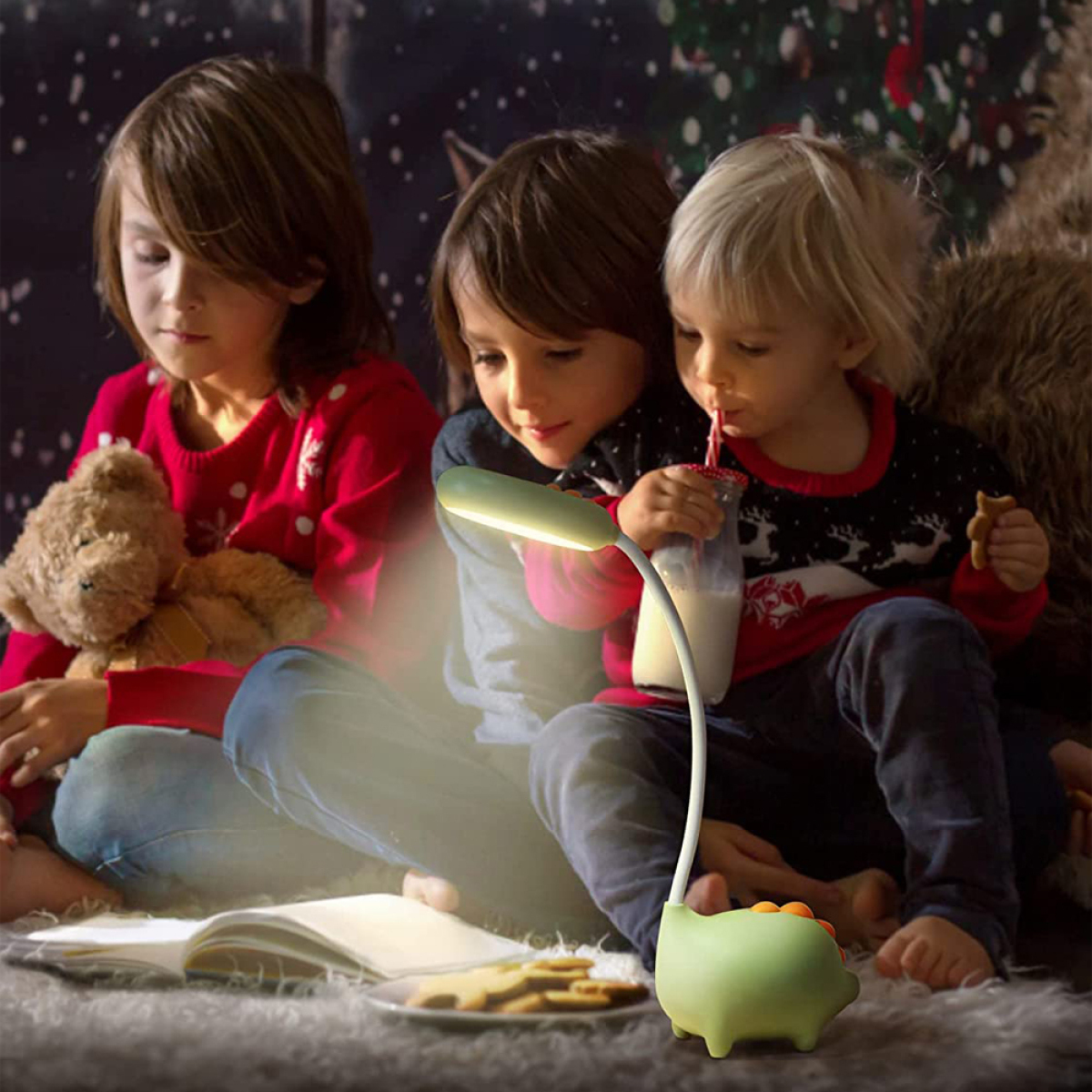 Drei Kinder sitzen, lesen und trinken, mit einer dinosaurierförmigen Lampe und Keksen.