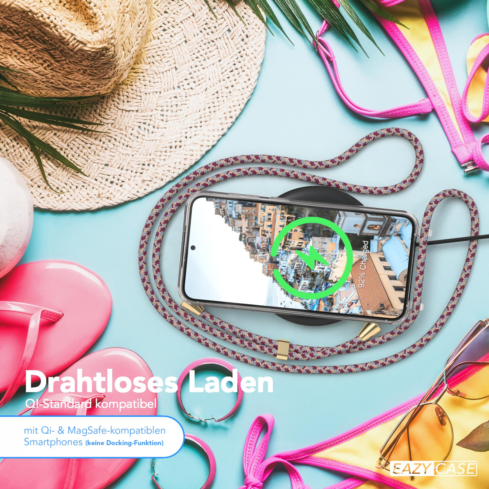 Telefon mit Kordel-Hülle auf einem kabellosen Ladegerät. Strandaccessoires im Hintergrund.