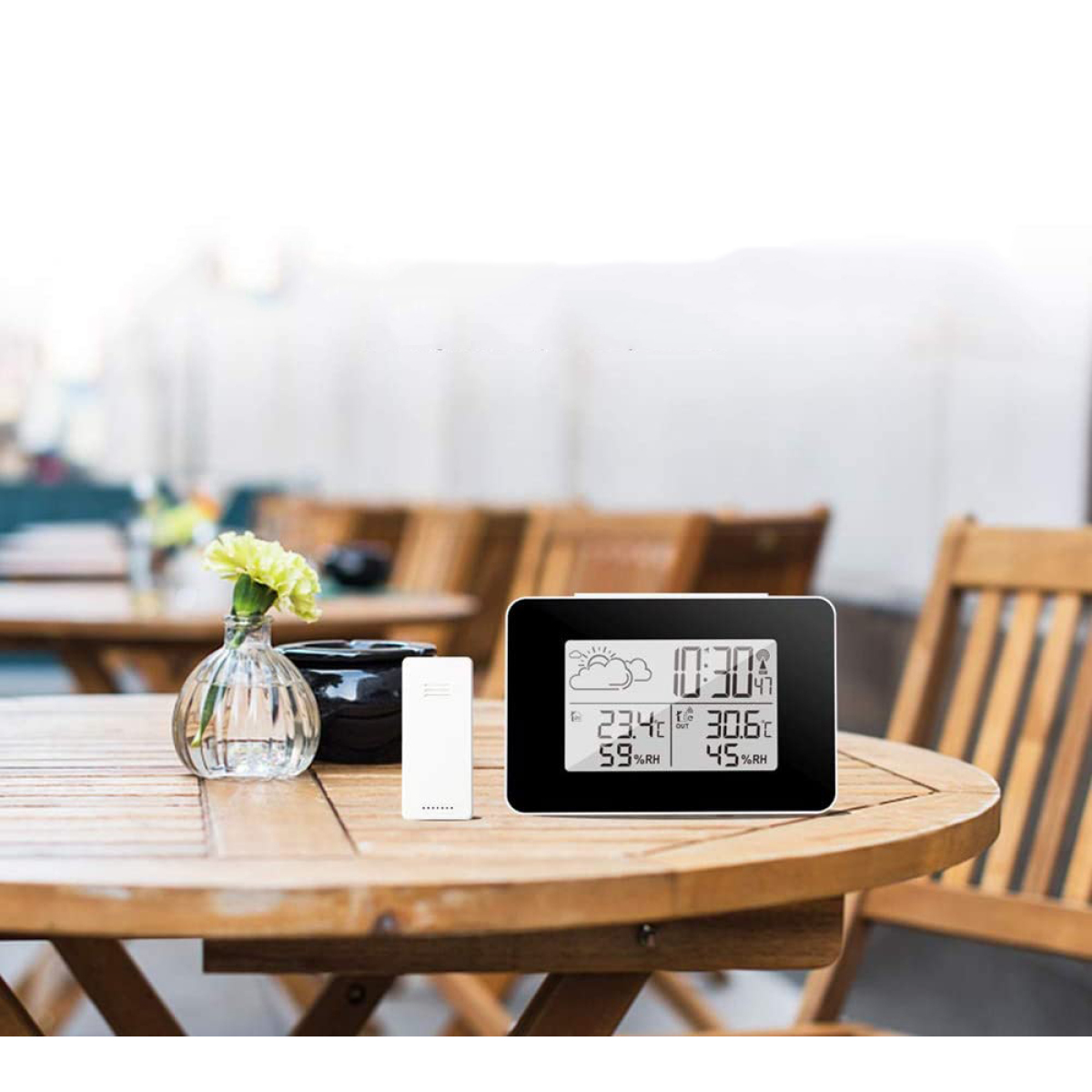 Eine Digitaluhr mit Uhrzeit und Wetterinformationen, mit einer Vase und einem kleinen weißen Sensor.