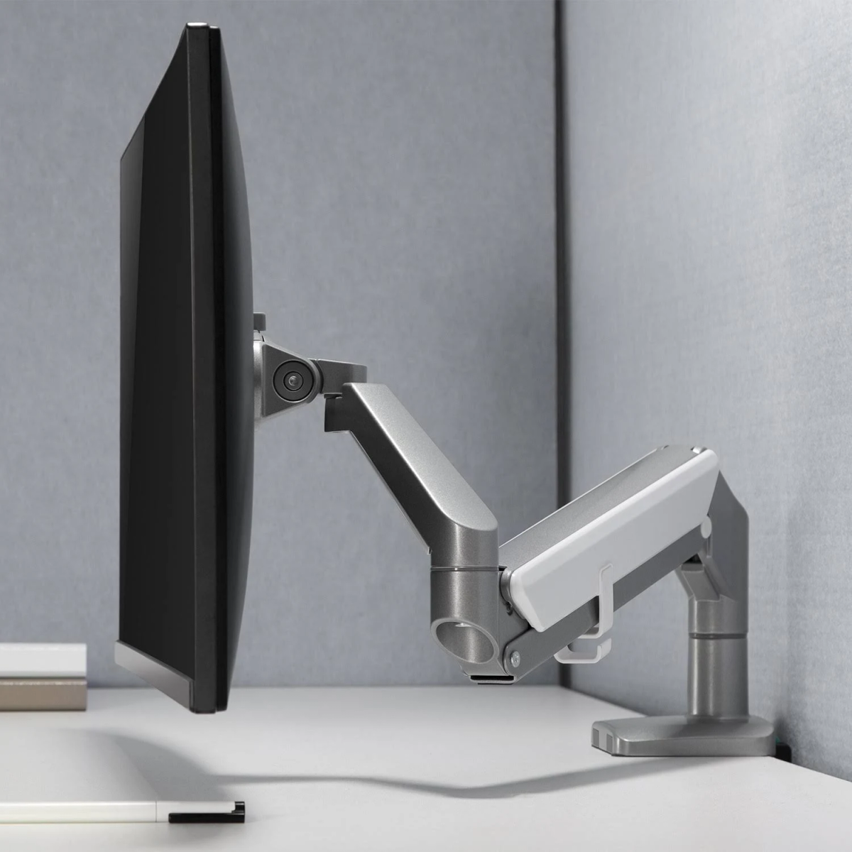 Ein Monitor, montiert an einem Gelenkarm, auf einem Schreibtisch mit weißer Oberfläche.