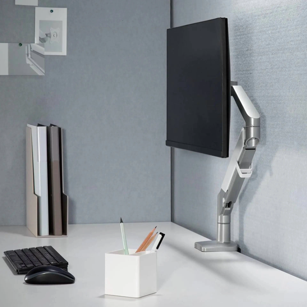 Ein Schreibtisch mit Monitorarm, Tastatur, Maus und einem Stifthalter mit Bleistiften. Links ist ein Aktenhalter.