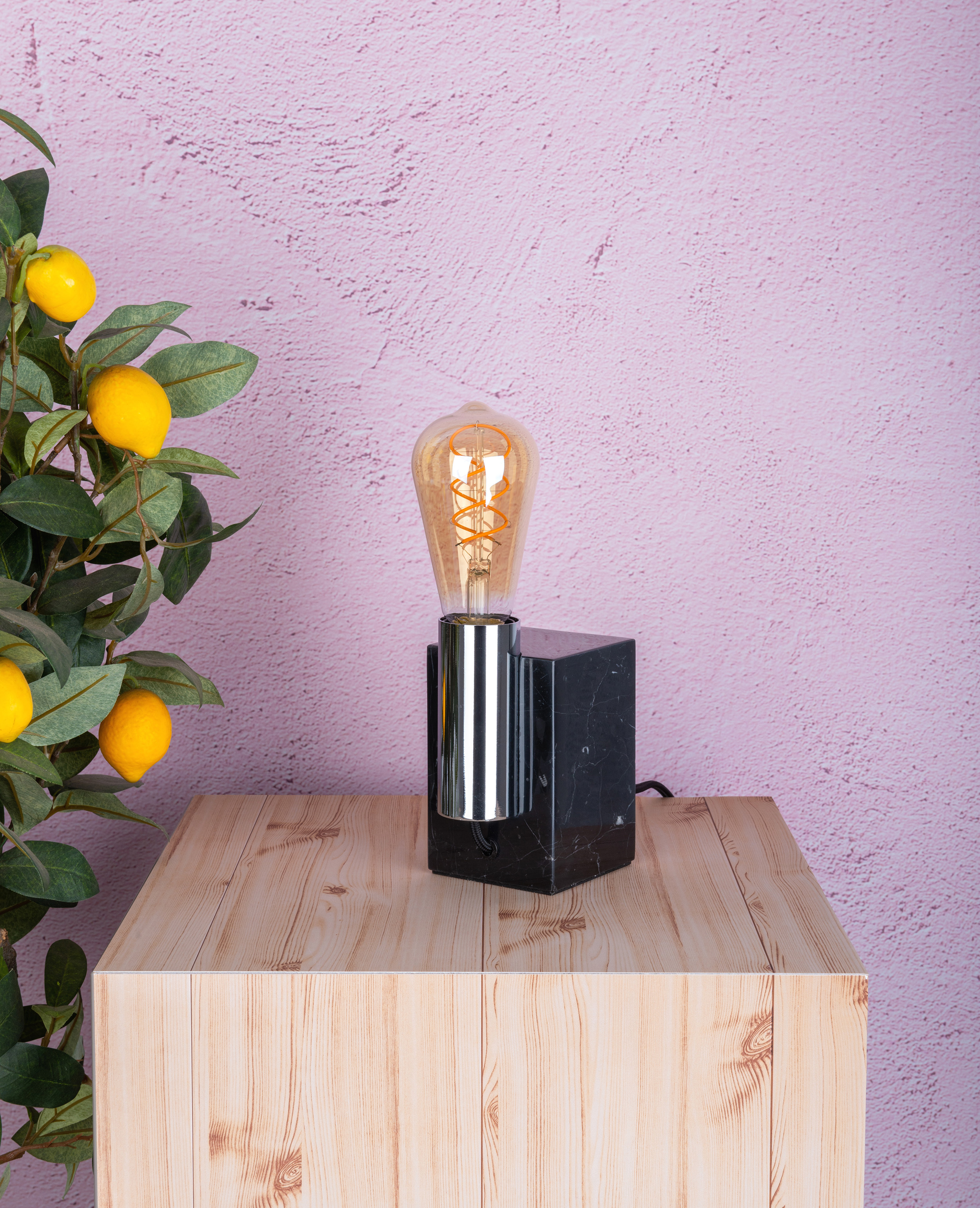 Eine moderne Tischlampe mit Glühbirne und schwarzem Sockel, auf einem Holztisch.