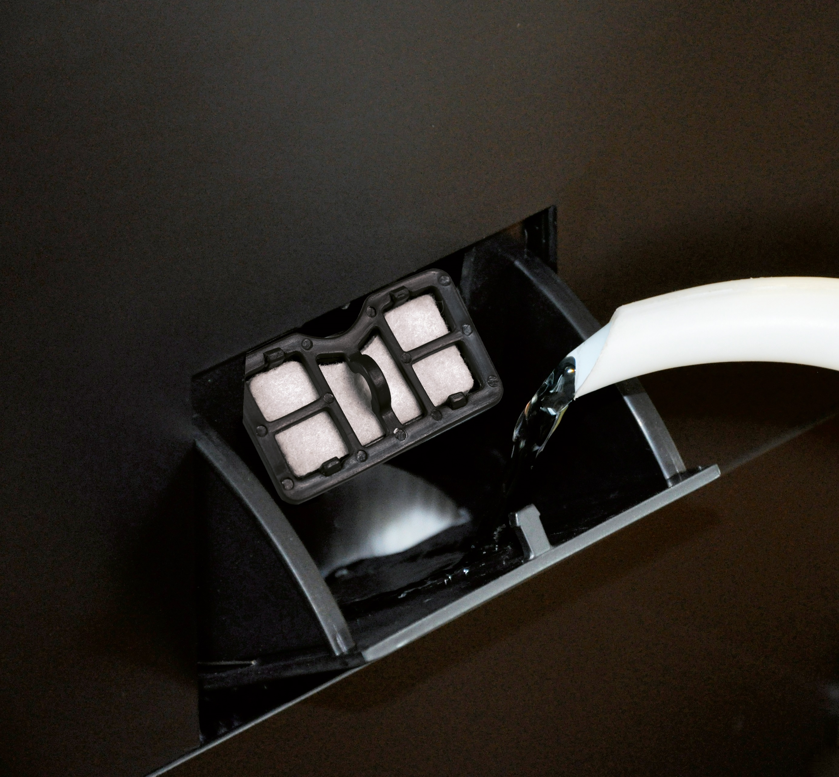 L'eau remplit un compartiment noir avec un filtre. Un tube blanc verse de l'eau. Le fond est noir.