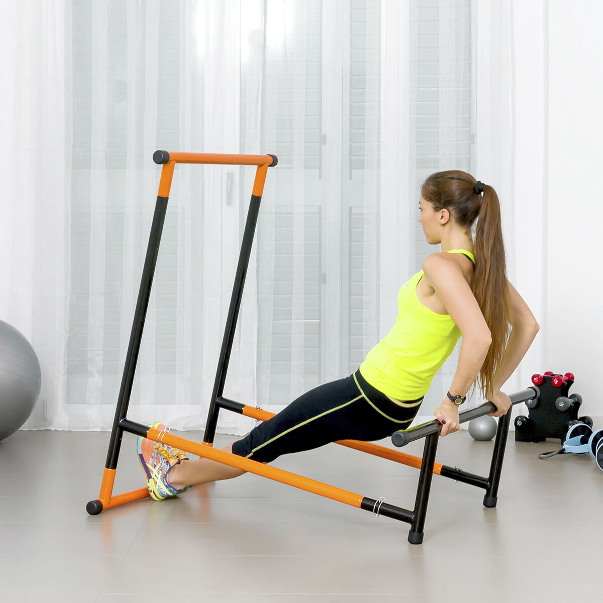 Mujer haciendo ejercicio en barras paralelas. Lleva top amarillo y mallas negras.