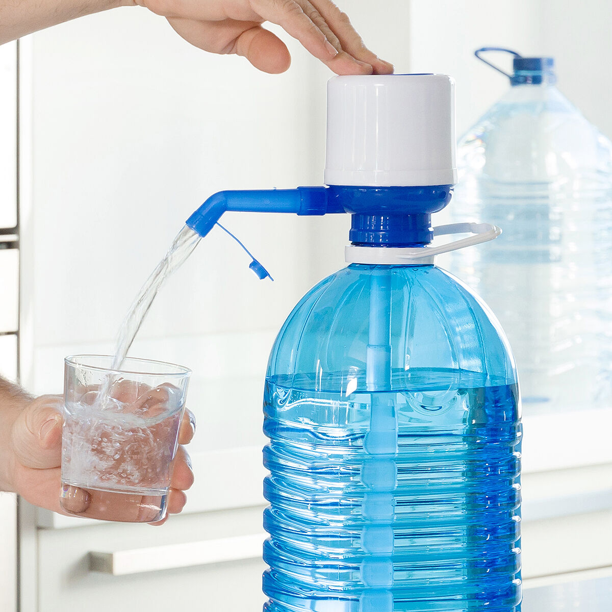 Eine Person gießt Wasser aus einer großen blauen Wasserflasche in ein Glas.