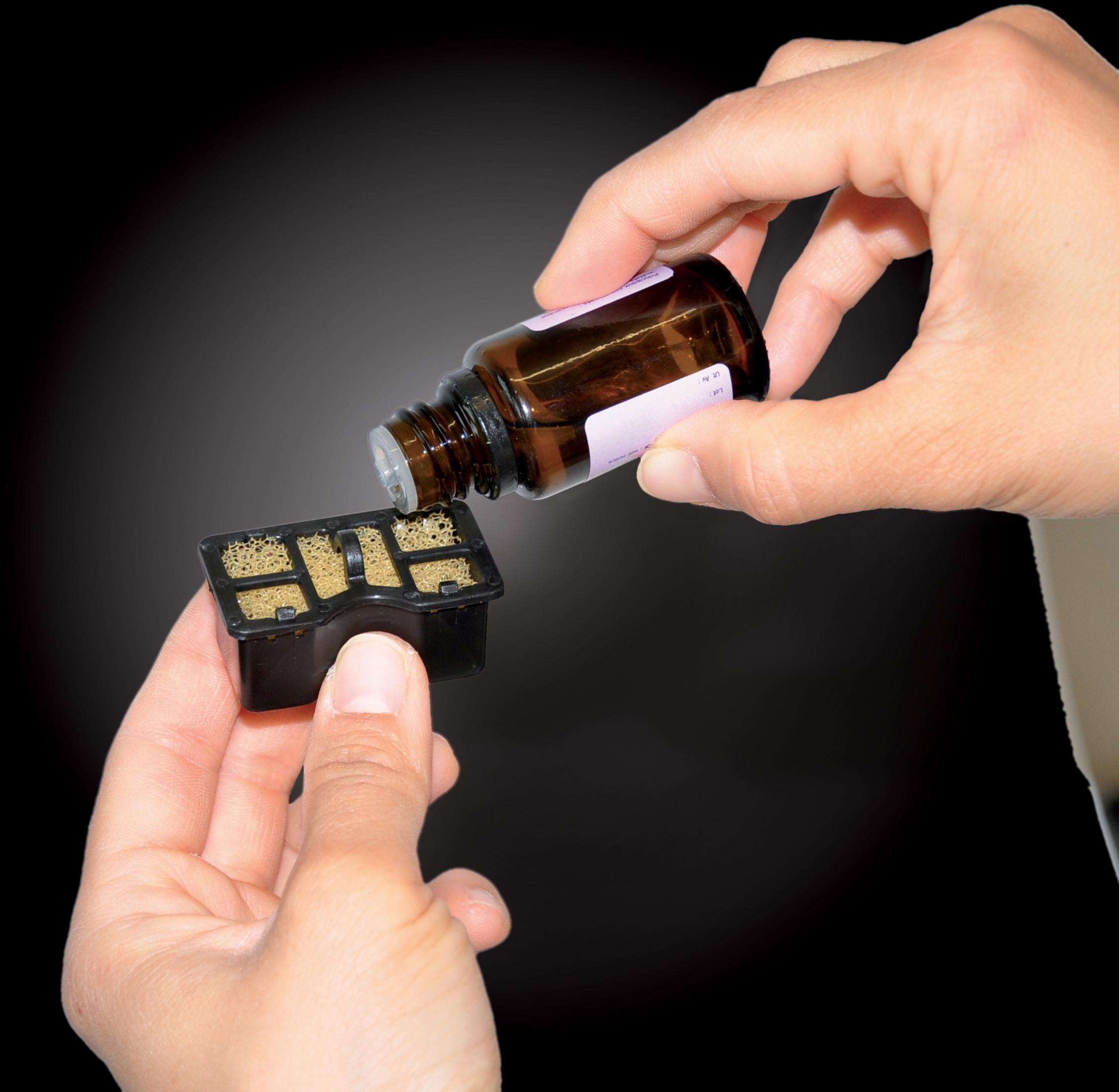 Hands pouring liquid from a brown bottle into a black container with yellow inserts.