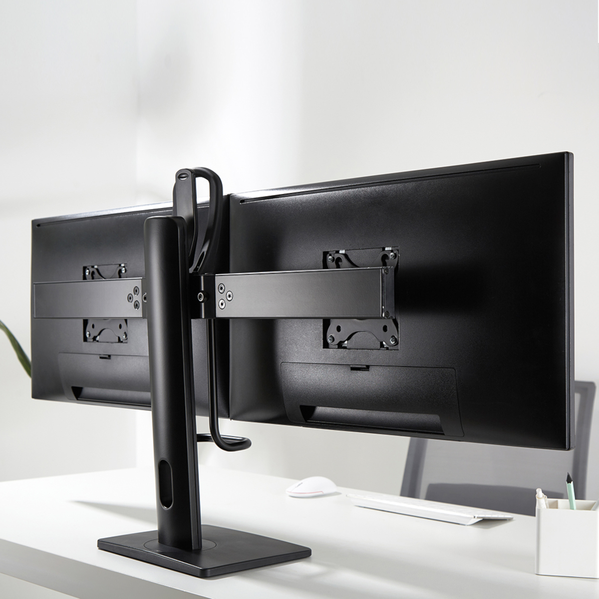 Rückansicht von zwei schwarzen Computermonitoren, die auf einem schwarzen Armständer stehen.