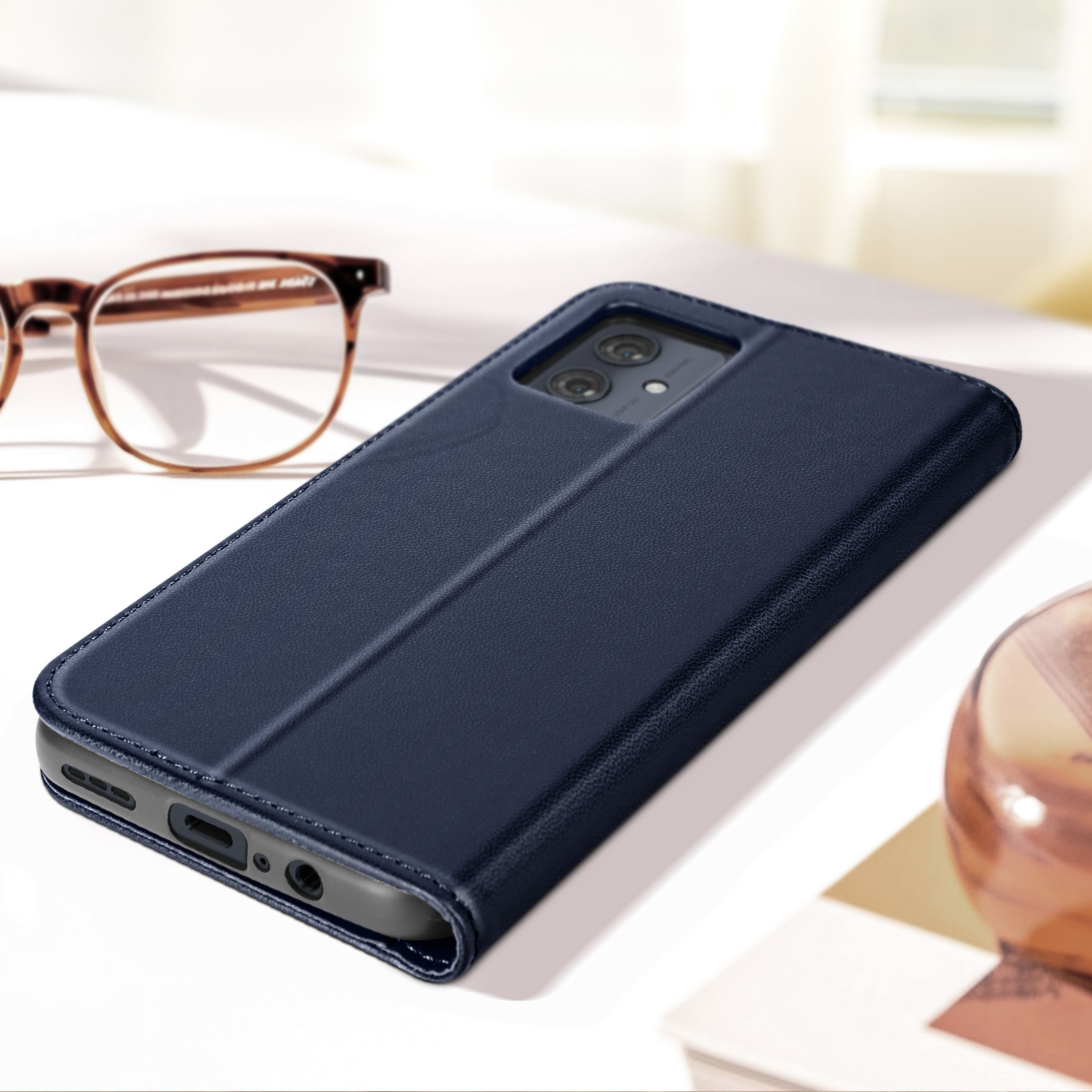 Eine blaue Leder-Handyhülle, geöffnet auf einer weißen Oberfläche, mit Brille im Hintergrund.