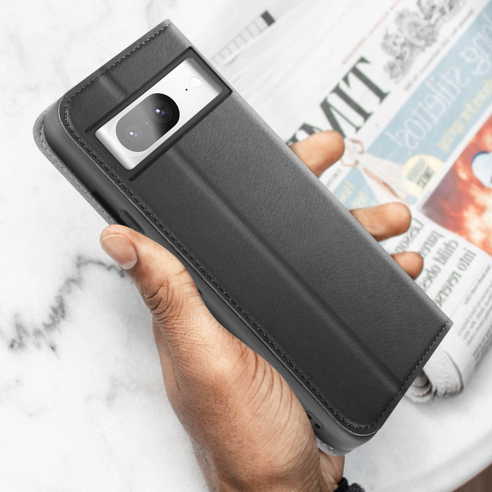 Eine schwarze Handyhülle mit einem Telefon darin, gehalten von einer Hand. Der Hintergrund ist eine Zeitung.