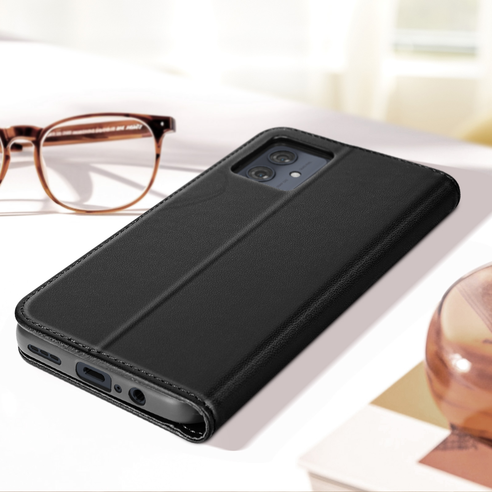 Schwarzes Telefon in einer Hülle auf weißer Oberfläche. Brille im Hintergrund.