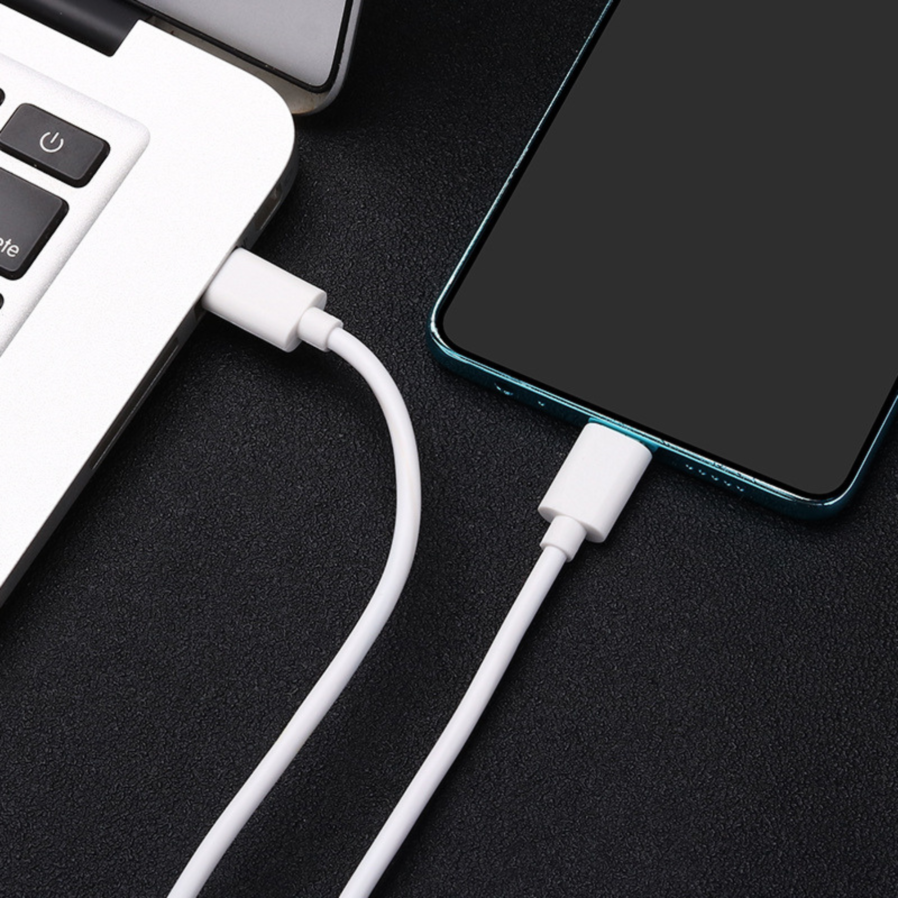 Ein weißes USB-C-Kabel, das mit einem Laptop und einem Smartphone verbunden ist, beide schwarz und blaugrün.