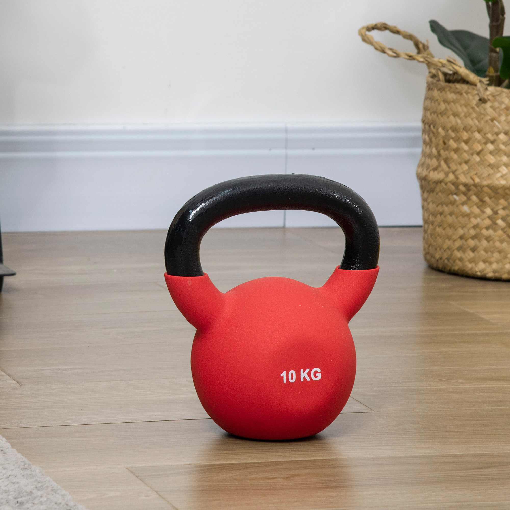 Pesa rusa roja de 10 KG en piso de madera. Fondo: pared blanca y canasta de mimbre.