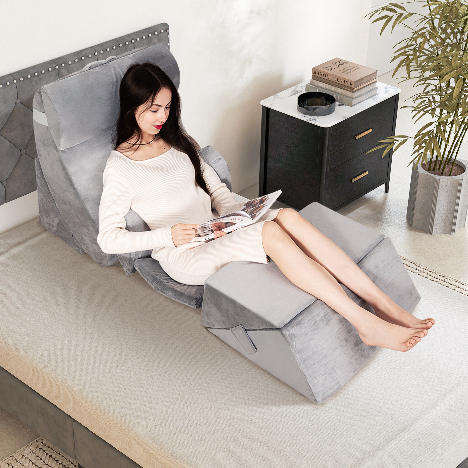 Frau in weißem Kleid liest auf verstellbarem grauem Bett mit Beistelltisch und Pflanze.