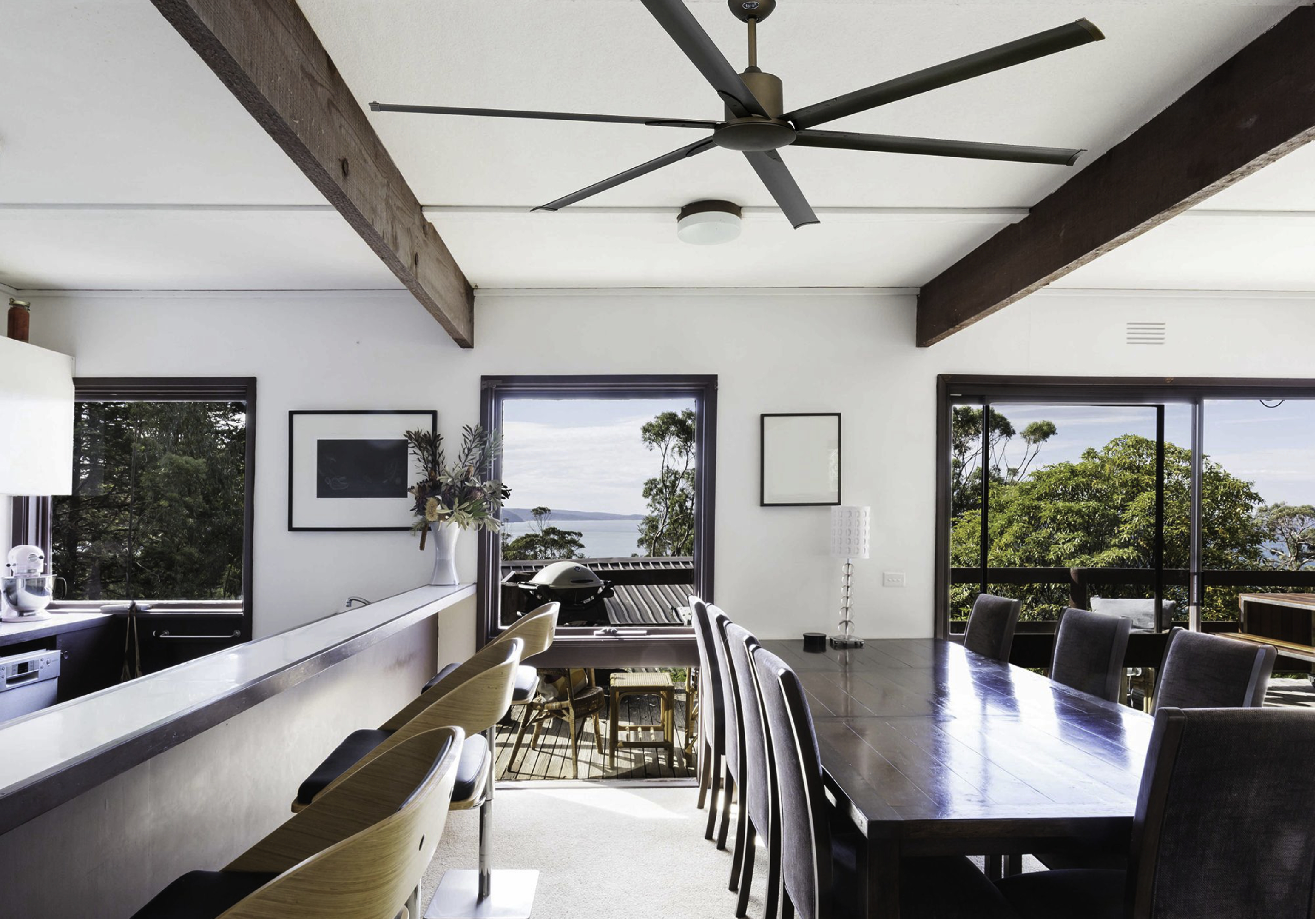 Una sala da pranzo con vista mare. Include un lungo tavolo di legno, sedie e un ventilatore a soffitto. Luminoso e arioso.