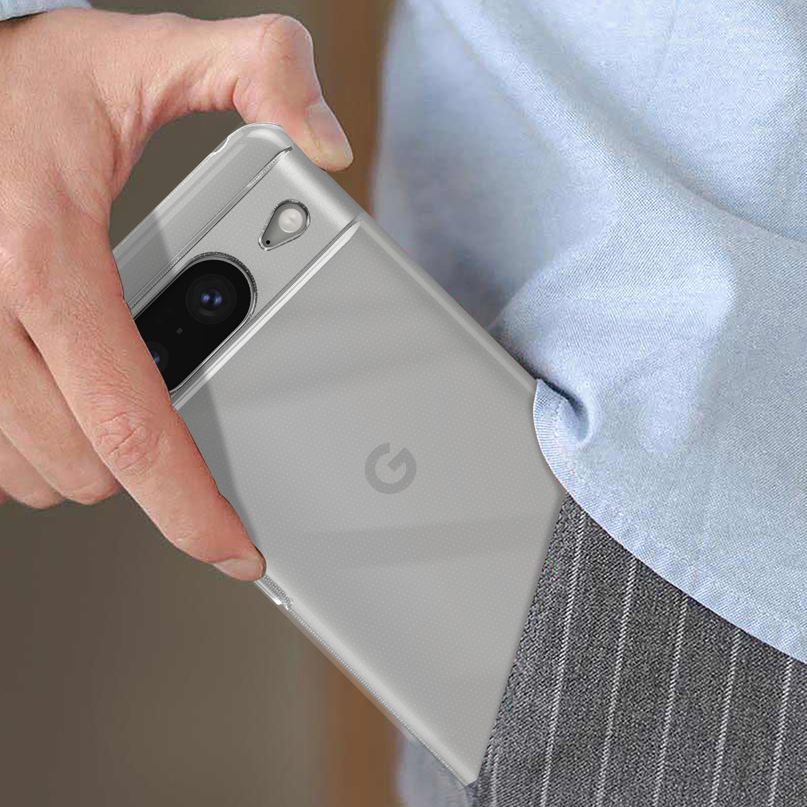 Hand hält silbernes Telefon. Telefon hat Kamera und G-Logo. Graue Hose mit gestreifter Tasche sichtbar.