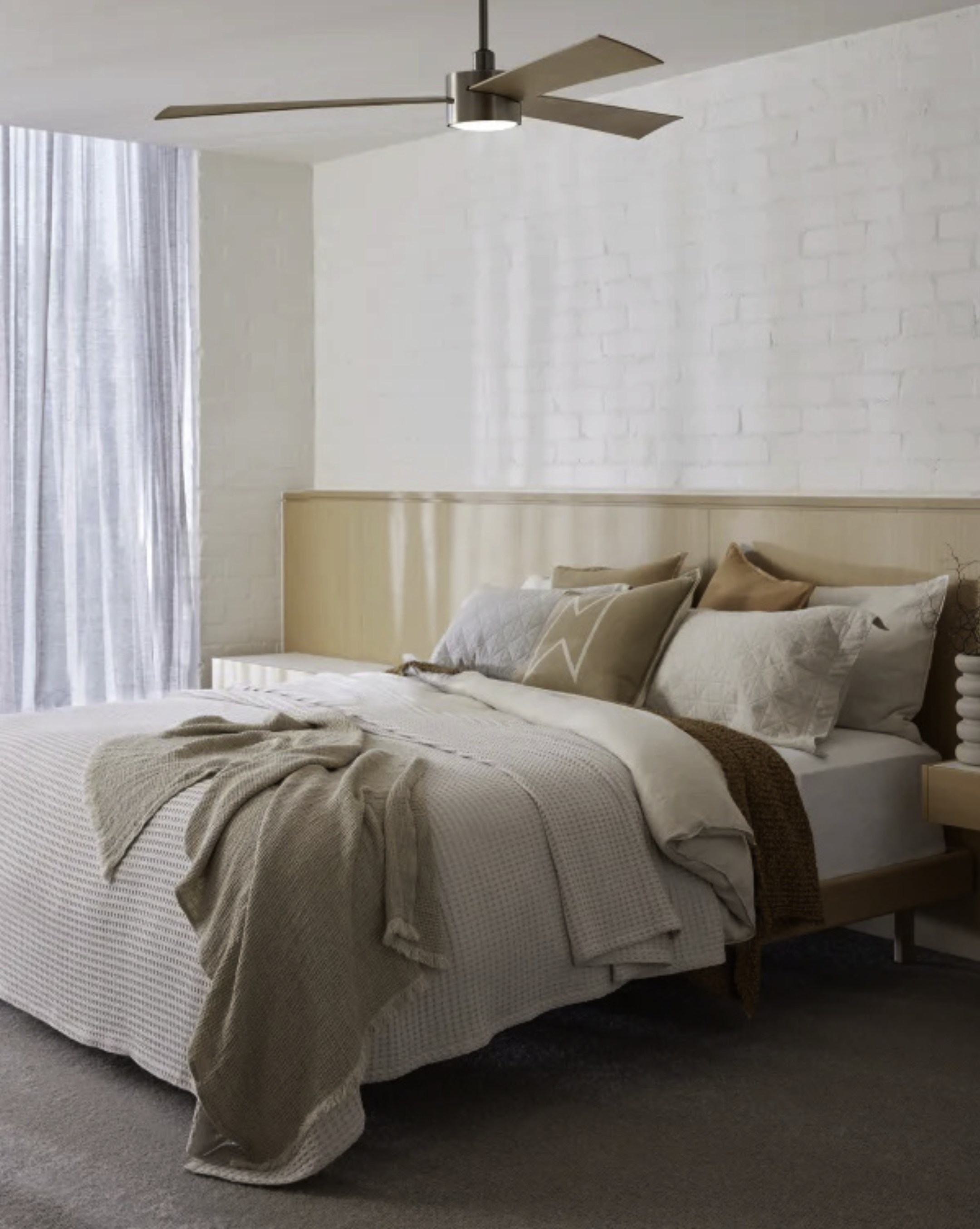 Schlafzimmer mit Bett, Kissen und Decke. Links ein Fenster mit Vorhang.
