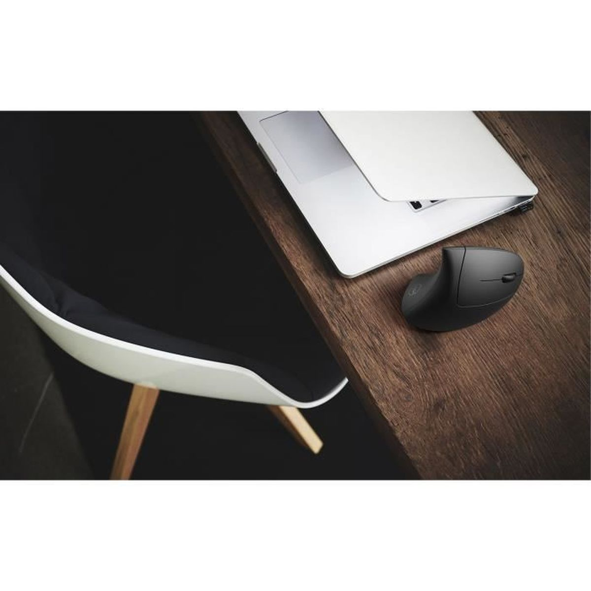 Un ratón ergonómico gris y una laptop en un escritorio de madera junto a una silla moderna.