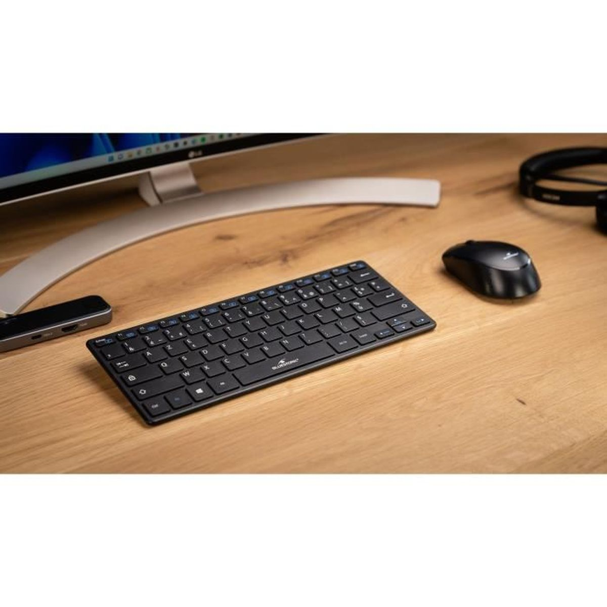 Eine kleine schwarze Tastatur und Maus auf einem Holzschreibtisch.