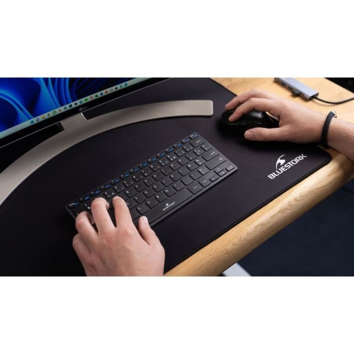 Eine Person benutzt eine schwarze Tastatur und Maus auf einem Schreibtisch. Das Mauspad.