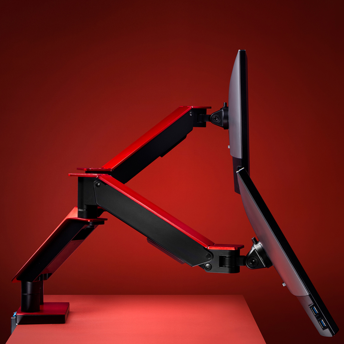 Ein Doppelmonitor-Setup, die Halterung ist rot und schwarz. Der Hintergrund ist rot. Die Monitore sind sichtbar.