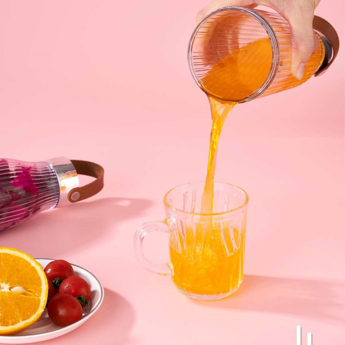 Eine Frau gießt Orangensaft in ein Glas mit Henkel; eine halbe Orange und Tomaten auf einem Teller.