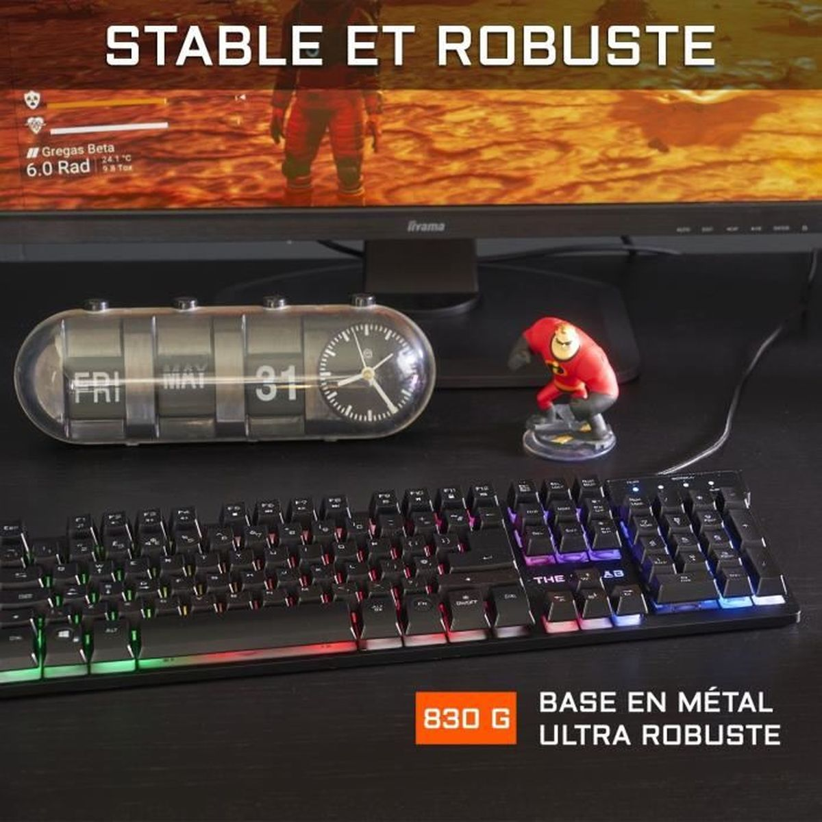 Eine Tastatur mit bunten Lichtern, eine Uhr, eine Figur und ein Monitor auf einem Schreibtisch.