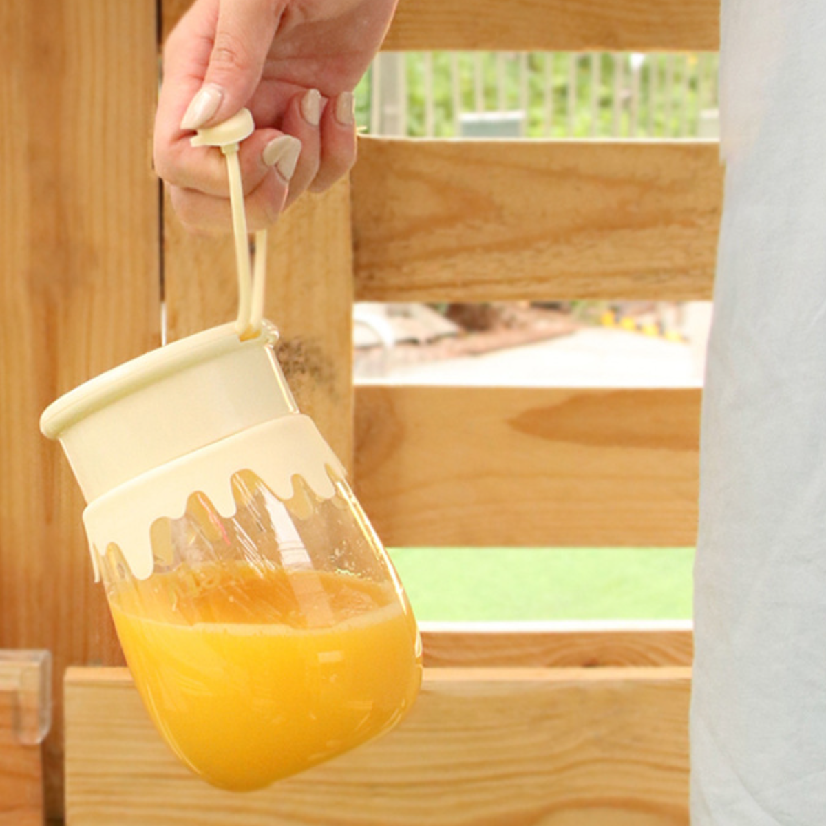 Hand hält ein klares Glas mit orangener Flüssigkeit. Das Glas ist weiß und hat ein dekoratives Tropfendesign.