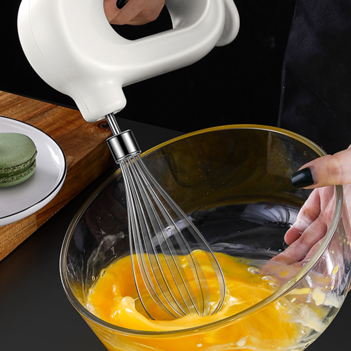 Eine Hand hält einen weißen elektrischen Mixer über einer Glasschüssel mit gelber Eimischung.
