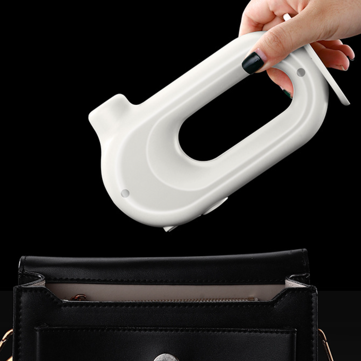 Eine Hand hält ein weißes Gerät und platziert es über einer offenen schwarzen Handtasche auf schwarzem Grund.