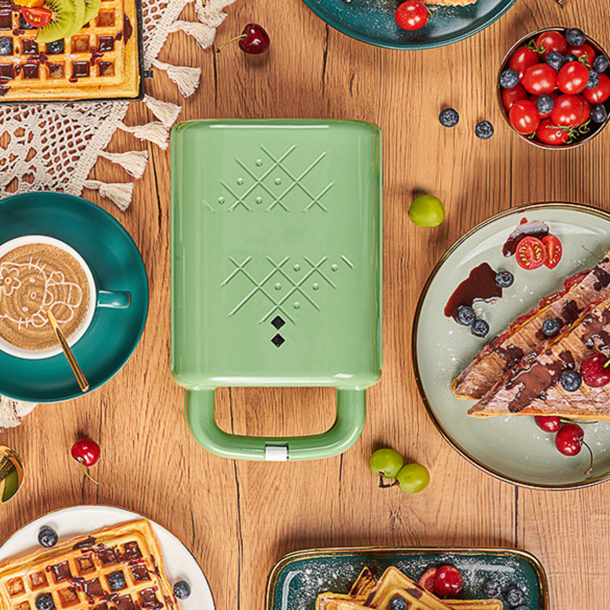 Grüner Waffeleisen mit Waffeln, Obst und Kaffee auf einem Holztisch.